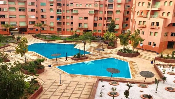 Ein Hotelinnenhof mit zwei Swimmingpools, umgeben von Palmen und Pflanzkästen.