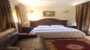 Ein Hotelzimmer mit einem großen Bett, einem Ledersofa, einem roten Teppich und einem Gemälde an der Wand.