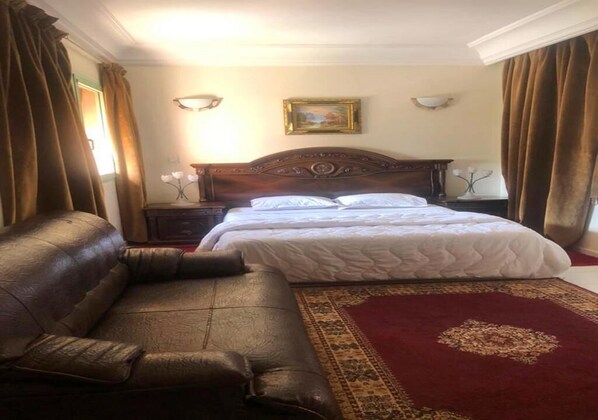 A hotel room with a large bed, a leather sofa, a red carpet, and a painting on the wall.