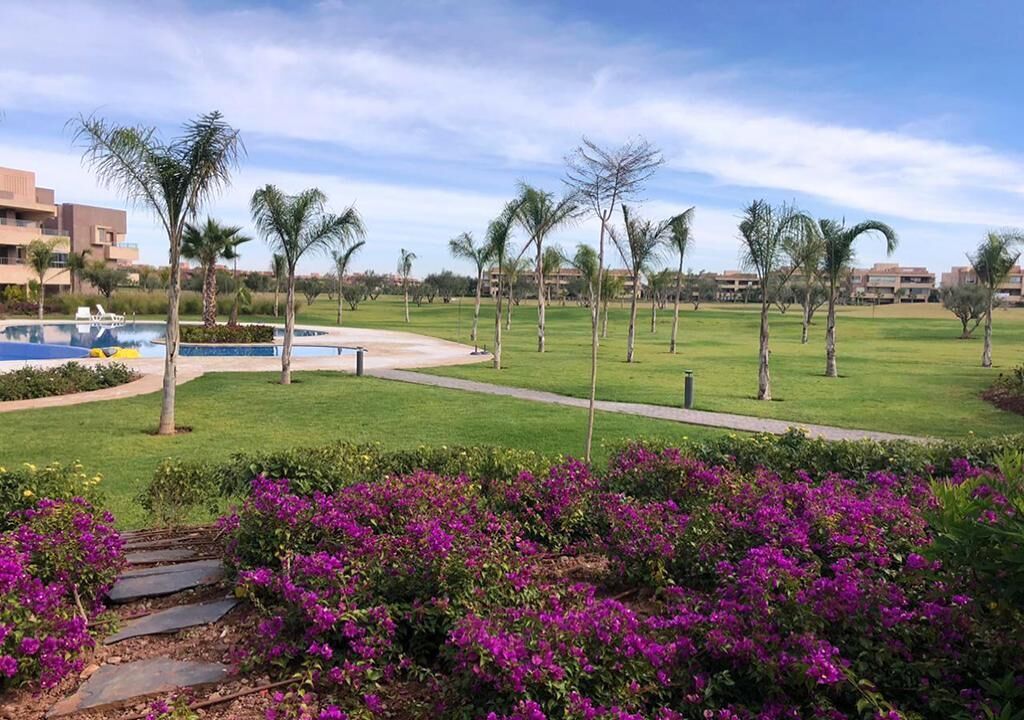 A resort with a swimming pool, palm trees, and purple flowers.