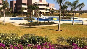 Un hotel moderno con piscina, palmeras y césped bien cuidado.