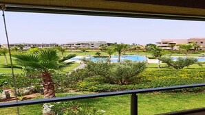 A view from a balcony overlooking a swimming pool and landscaped garden with palm trees and shrubs. - Residence Marrakech Prestigia Golf City 5304 (Marrakech)