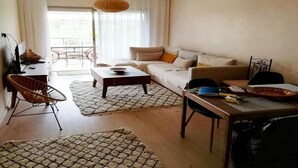 A living room with a sofa, coffee table, and dining table. There is a chair, a lamp, and a window with curtains. - Residence Marrakech Prestigia Golf City 5304 (Marrakech)