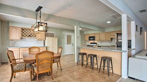 A spacious kitchen with a dining area, featuring a central island with stools, wooden cabinets, and a hanging light fixture. - Possum Kingdom Lakefront Home w/ Patio & Dock! (Graford)