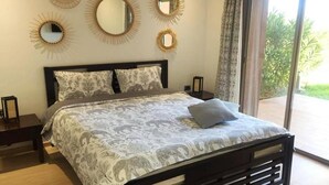 A bedroom with a bed, two nightstands, and a large window with a view of greenery.