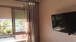 Una stanza con un letto, una TV a muro, una finestra con tende e vista sul verde.