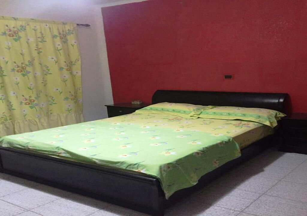 A room with a bed, a nightstand, a red wall, and a floral curtain.