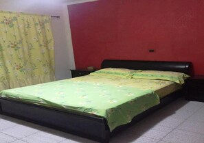 A room with a bed, a nightstand, a red wall, and a floral curtain.
