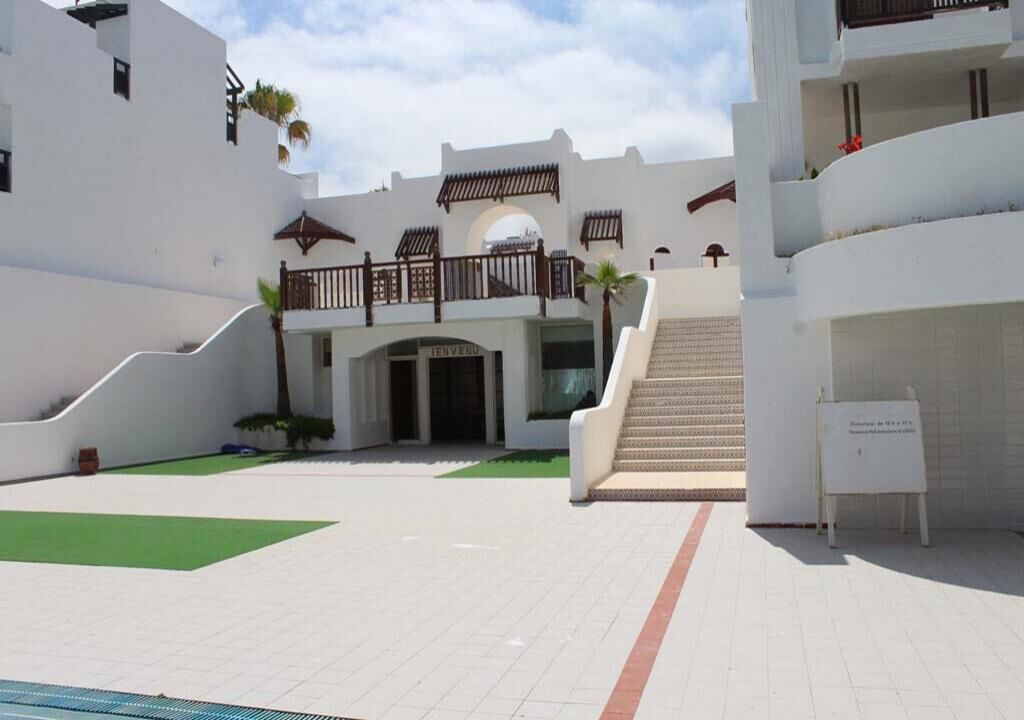 Un bâtiment moderne doté d’une entrée centrale, d’un escalier menant à un balcon et d’une enseigne.