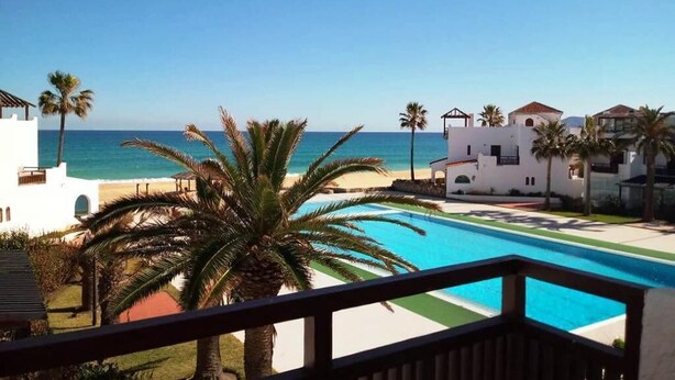 A resort with a pool, palm trees, and a view of the sea.