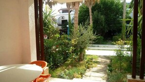A patio area with a table and chairs, surrounded by lush greenery and a pathway leading to a white vehicle.