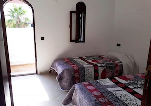 Una habitación con dos camas, un espejo pequeño y una puerta que da al exterior.