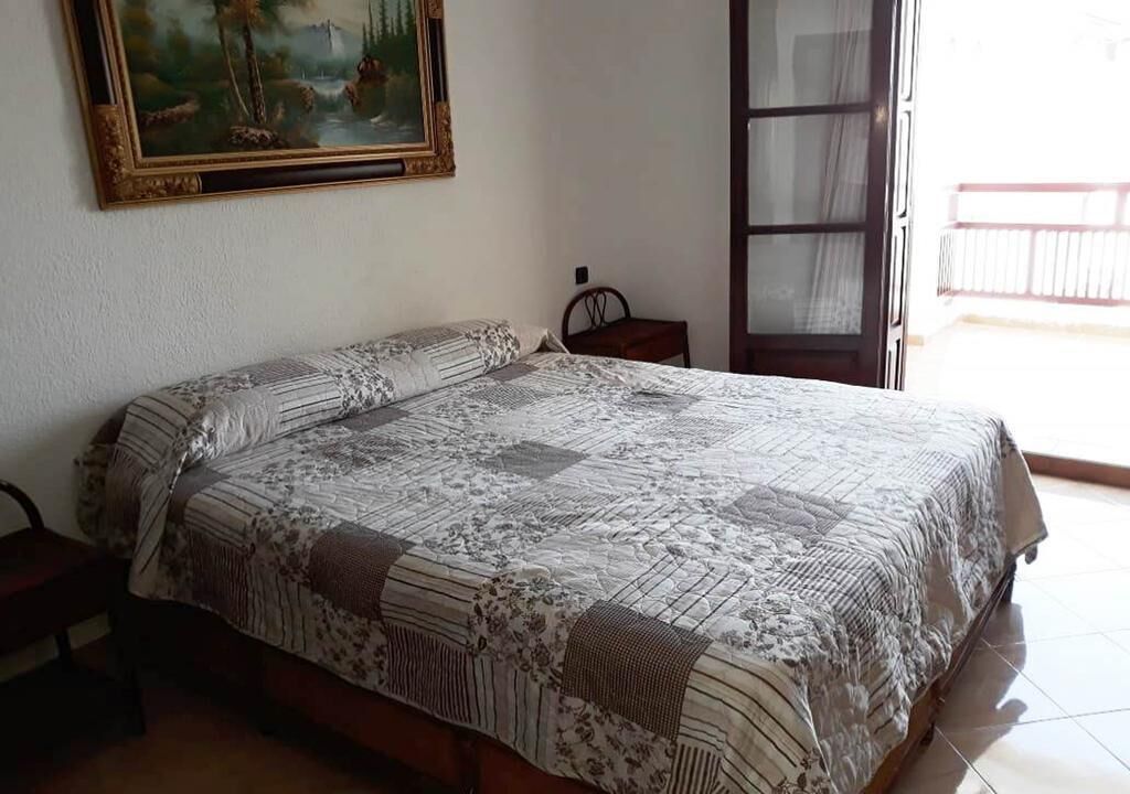 A bedroom with a bed, a nightstand, a chair, and a painting on the wall.