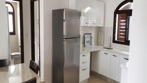 Une cuisine moderne avec des meubles blancs, un réfrigérateur en acier inoxydable, un évier et une fenêtre équipée de stores.
