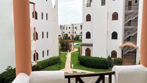 Une vue depuis un balcon donnant sur une cour intérieure, avec des bâtiments blancs, une piscine et un escalier.
