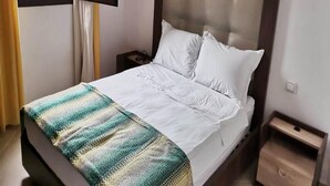 Un lit bien fait, avec des draps blancs, une couverture à rayures et une tête de lit en bois.
