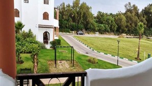 A white building with a balcony, a grassy area with a swing set, and a road in the background. - Residence Mangle 5332 (Cabo Negro)