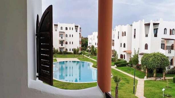 A view of a pool surrounded by white buildings with balconies, a clear sky, and a well-maintained lawn. - Residence Mangle 5332 (Cabo Negro)