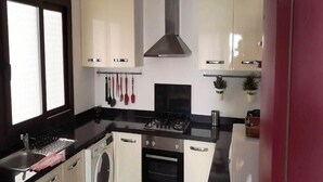 A compact kitchen with a gas stove, oven, washing machine, and a sink. - Residence Mangle 5332 (Cabo Negro)