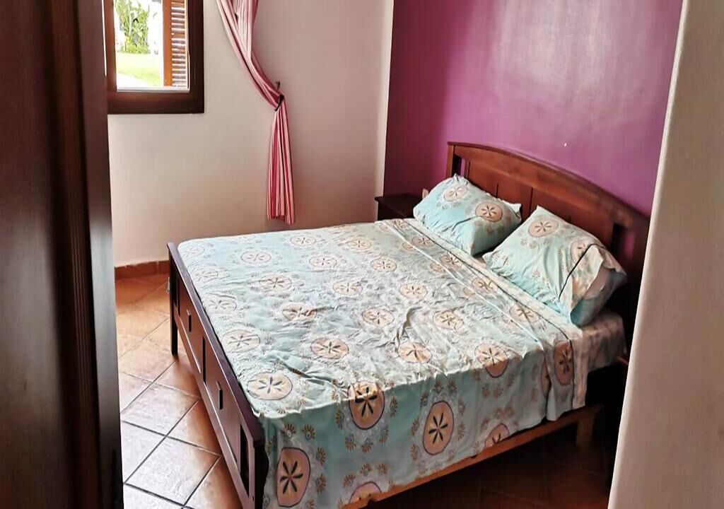 A bedroom with a bed, a window with curtains, and a purple wall.
