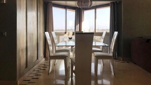 A dining area with a glass table and chairs, large windows offering a city view, and a modern pendant light.
