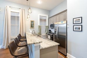 A modern kitchen with a marble countertop, stainless steel appliances, and a seating area with chairs.