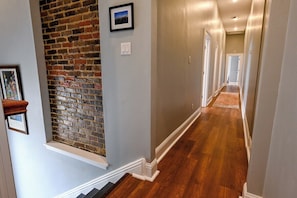A hallway with a brick accent wall, a wooden floor, and a picture frame on the wall.