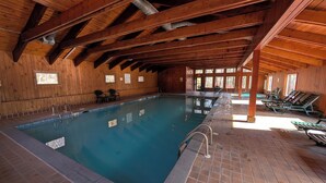 Une piscine intérieure avec des poutres en bois, un sol carrelé et de grandes fenêtres laissant entrer la lumière du soleil.