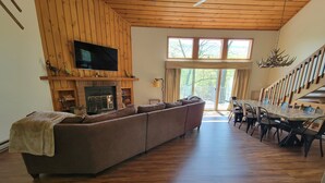 Un salon spacieux avec un grand canapé, une cheminée et un coin repas comprenant une longue table et des chaises.