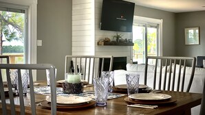 A dining area with a wooden table set for four, a ceiling fan, and a flat-screen TV mounted on the wall. - Hooked on Bayou? Waterfront! Kayaks, Fishing, Dock, The Views! (Carrabelle)