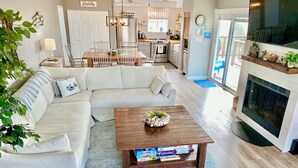 A living room with a sofa, coffee table, and fireplace. There is a kitchen in the background with a dining area. - Hooked on Bayou? Waterfront! Kayaks, Fishing, Dock, The Views! (Carrabelle)