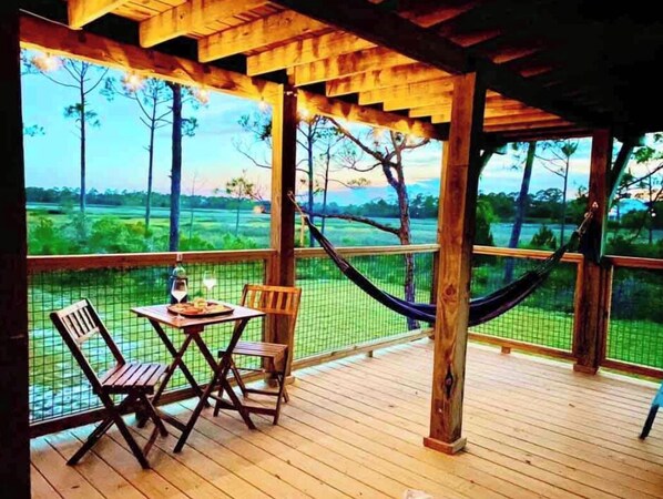 Una terraza de madera al aire libre con una mesa y sillas, con vista a un paisaje verde con árboles y una cerca.