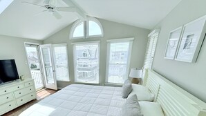 A bedroom with a large bed, a TV on a dresser, and multiple windows with blinds.