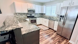A modern kitchen with white cabinets, a granite countertop, a stainless steel refrigerator, and a wood floor.