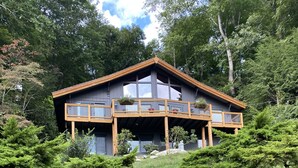 Een modern huis met twee verdiepingen, een houten terras en grote ramen.