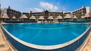 A large swimming pool with a curved edge, surrounded by thatched-roof structures and a modern building in the background. - Vietsovpetro Dalat Hotel (Da Lat)