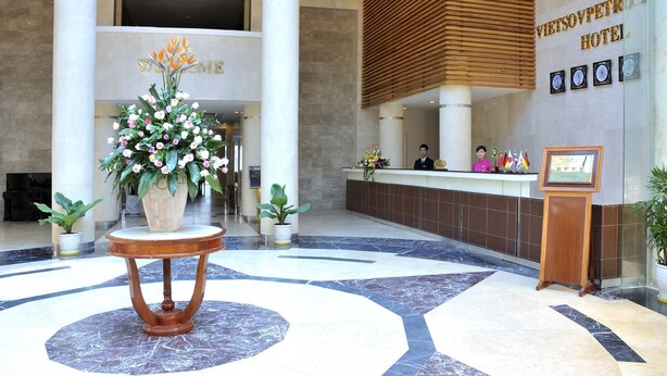 A hotel reception area with a marble floor, a large welcome sign, a reception desk, and a wooden slatted wall. - Vietsovpetro Dalat Hotel (Da Lat)