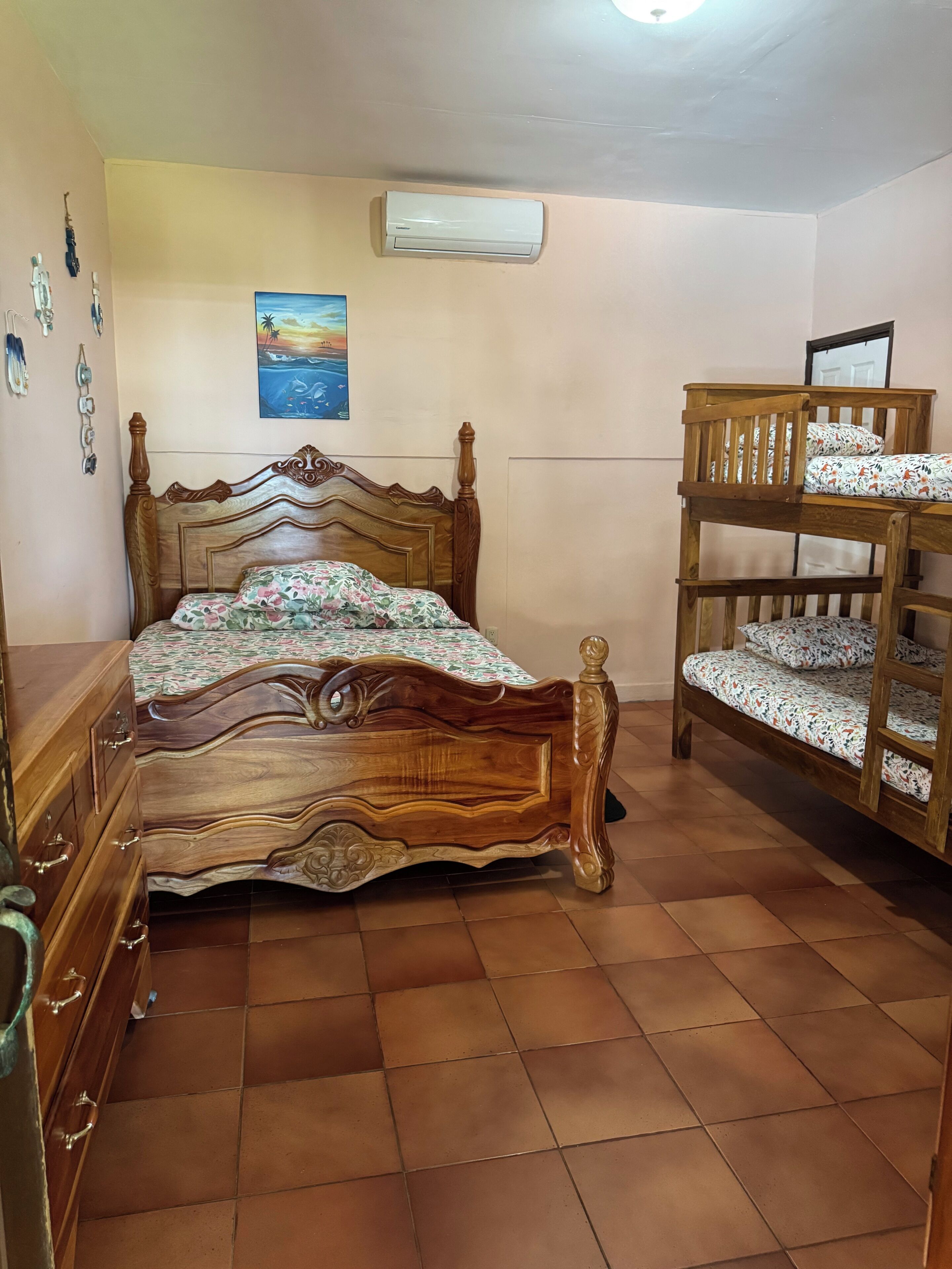 Une chambre à coucher avec un lit en bois, une commode, un lit superposé et un climatiseur fixé au mur.