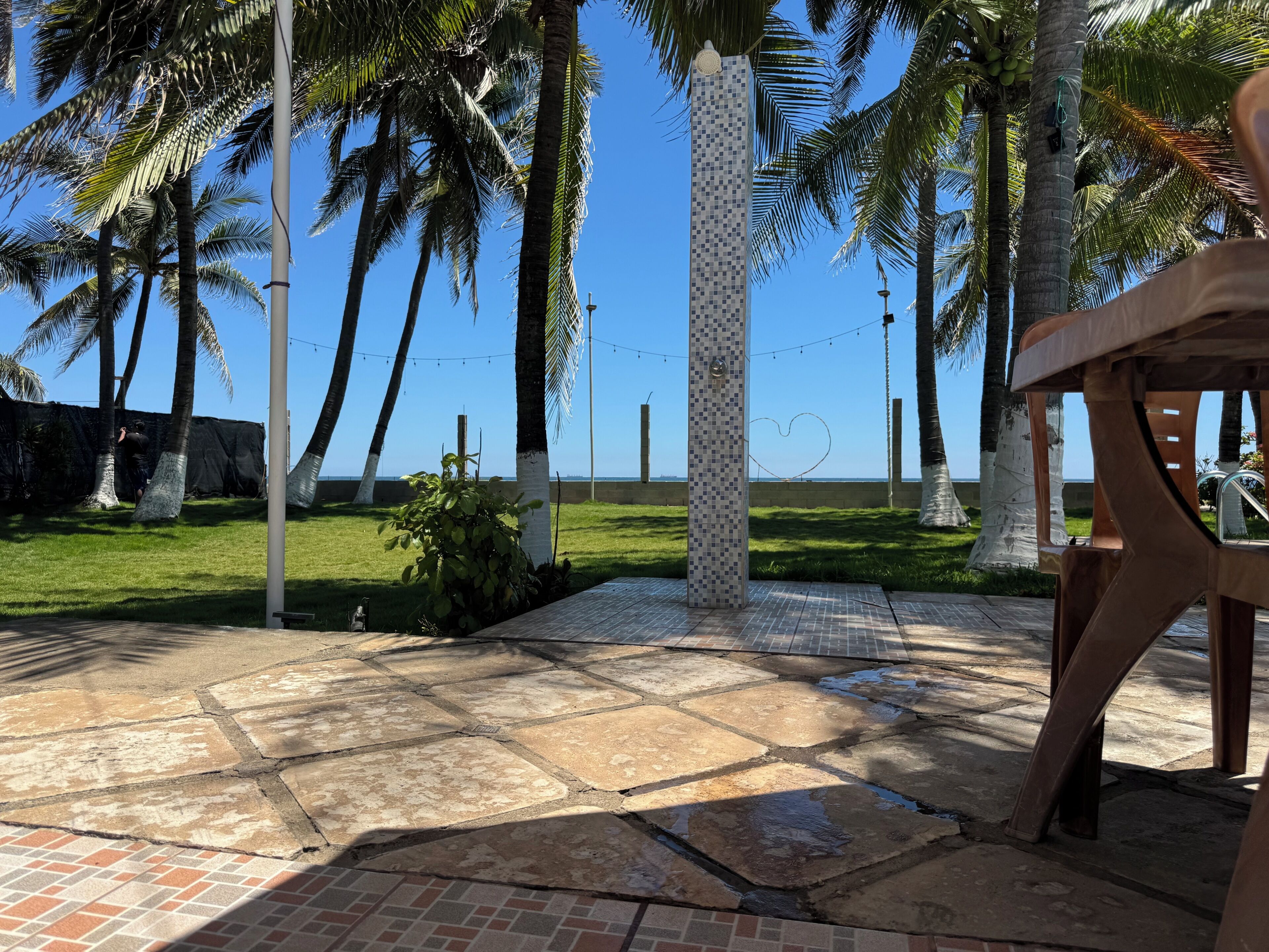 Un espace extérieur aménagé en patio, avec des palmiers, un sol carrelé et une vue sur l’océan.