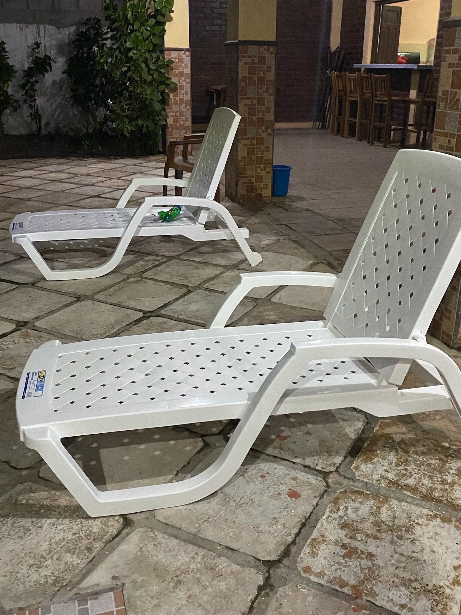 To hvide plastliggestole med perforerede rygge og sæder, placeret på en fliseterrasse.