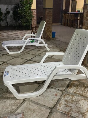 Two white plastic lounge chairs with perforated backs and seats, placed on a stone-tiled patio.