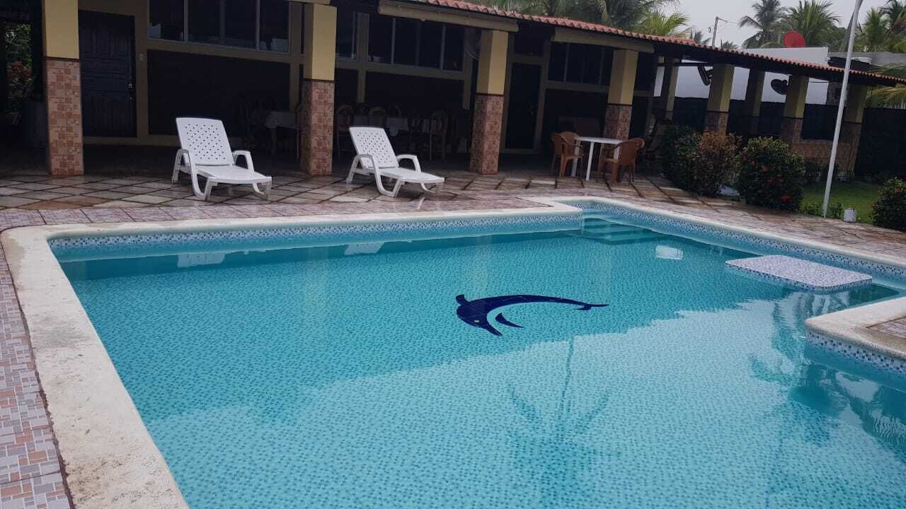 Ein Schwimmbecken mit einem Delphin-Logo, umgeben von Liegestühlen und einer überdachten Terrasse.