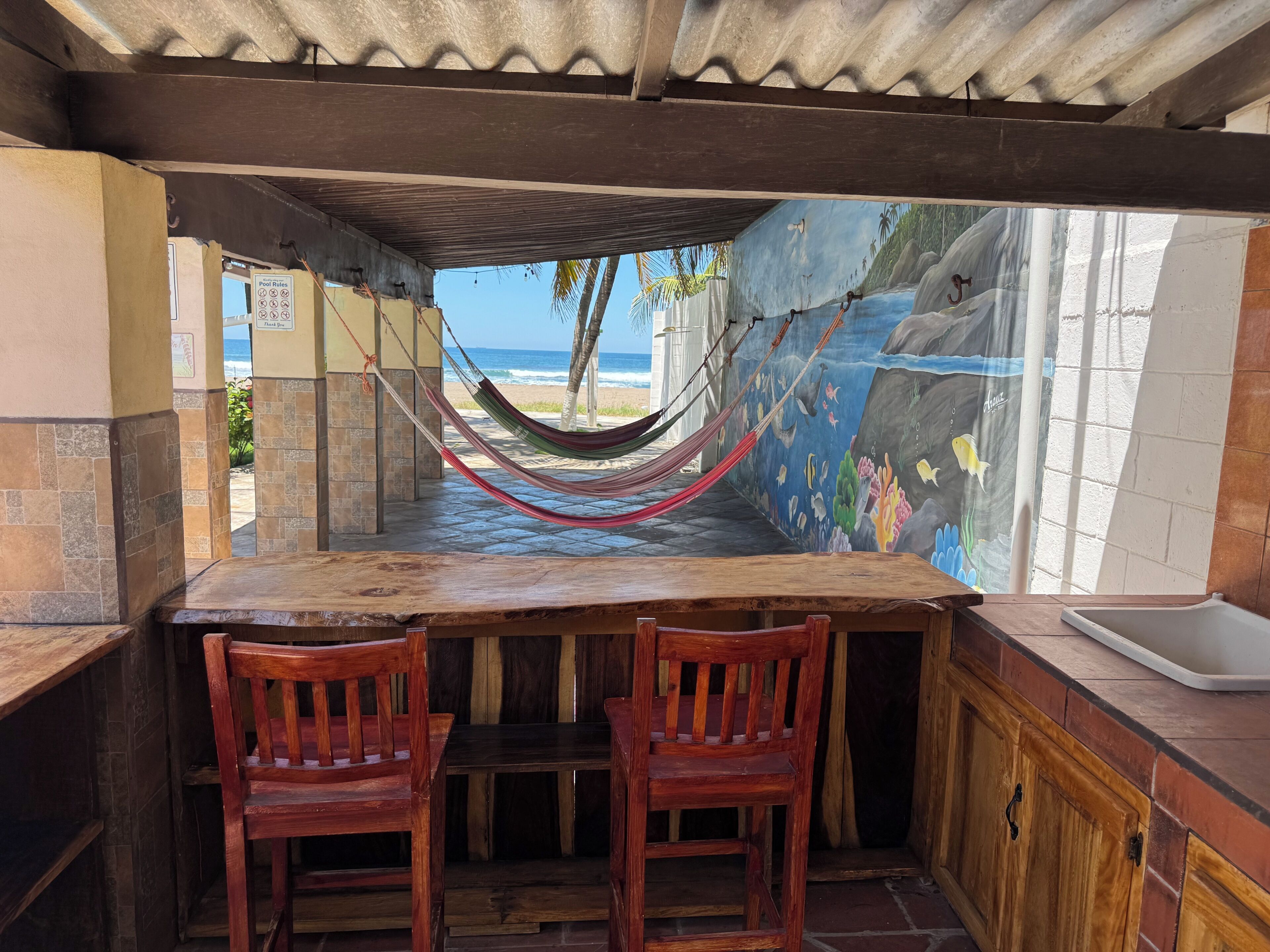 A wooden table with two chairs, a hammock, and a mural of a beach scene.