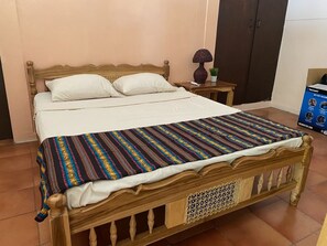 A wooden bed with white bedding, a colorful striped blanket, and a small bedside table with a lamp.