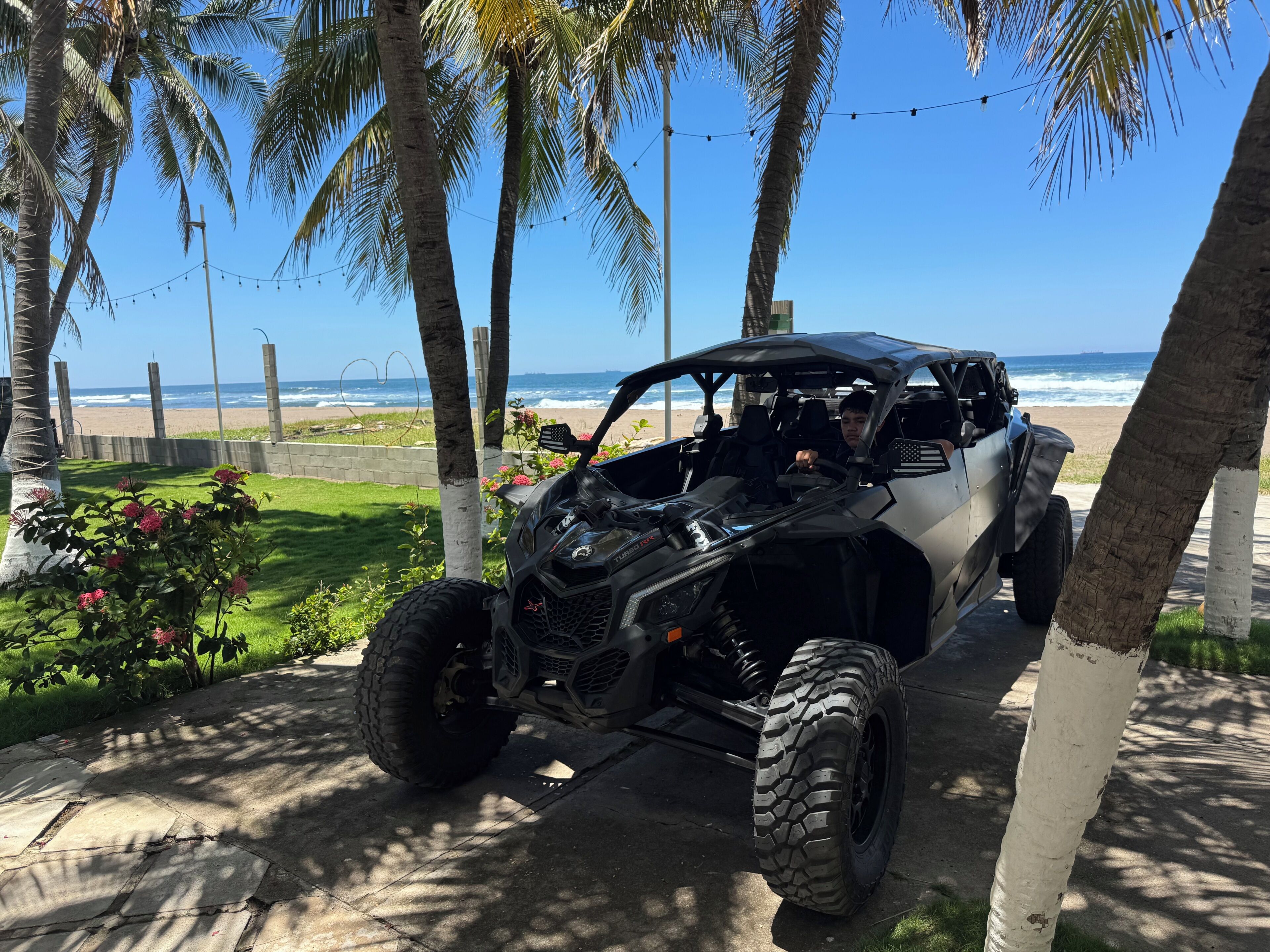 Een zwarte terreinwagen geparkeerd op een verhard pad, met een strand en de oceaan op de achtergrond.