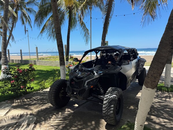 Un vehículo todoterreno negro estacionado en un camino pavimentado, con una playa y el océano al fondo.