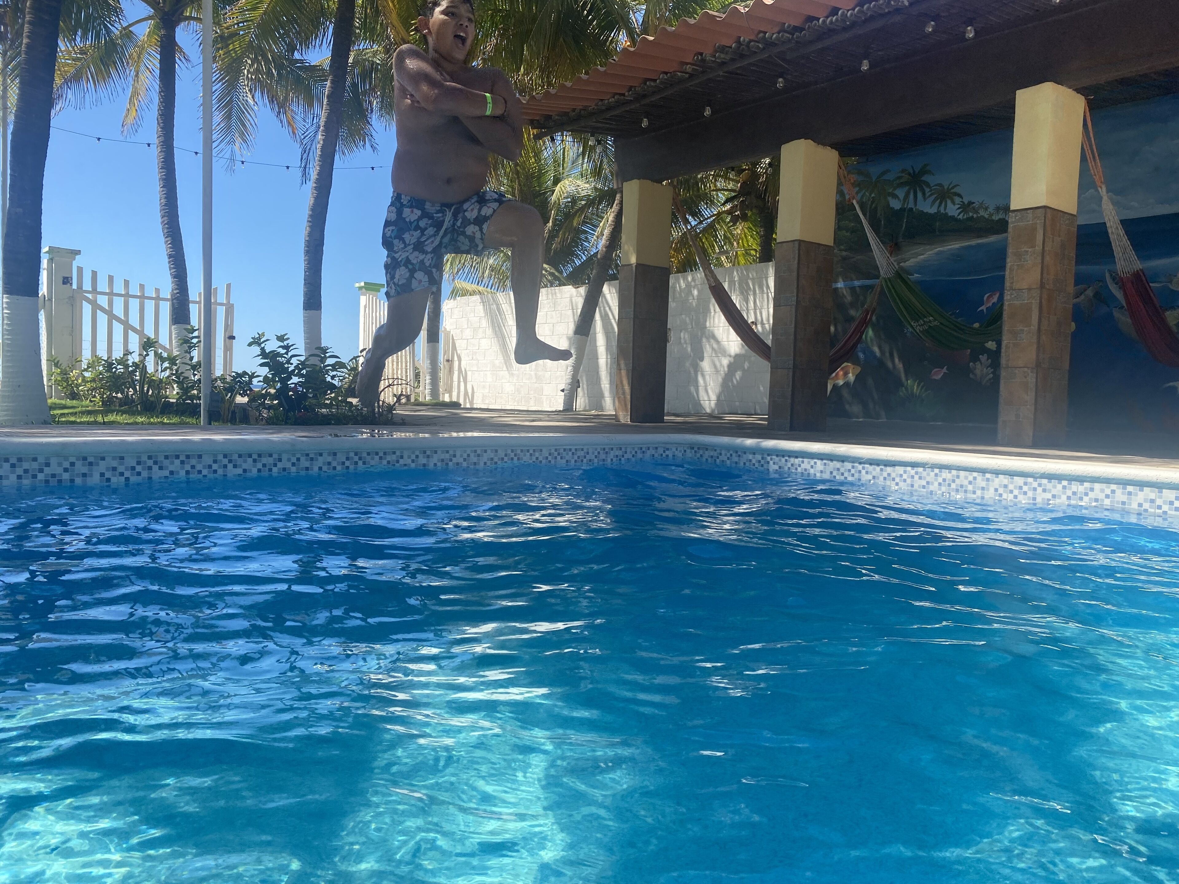 Una piscina con agua azul cristalina, rodeada de palmeras y un solárium con baldosas.