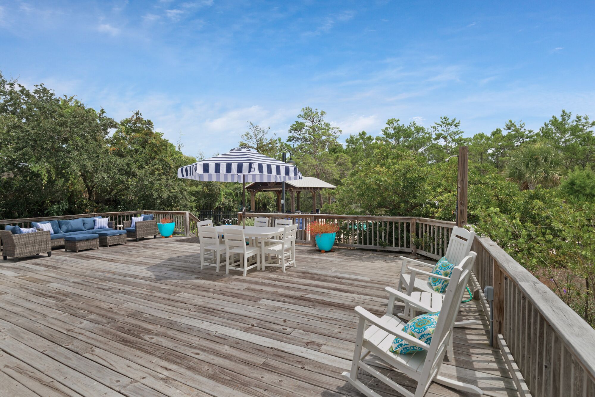A wooden deck with outdoor furniture, including sofas and chairs, and a striped umbrella.