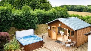 Een houten chalet met een jacuzzi en een terras met stoelen en een tafel.