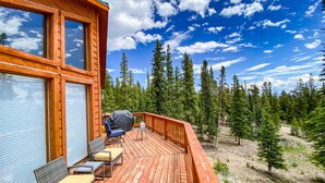 Une terrasse en bois avec des sièges d’extérieur, un barbecue et une vue sur une zone boisée.